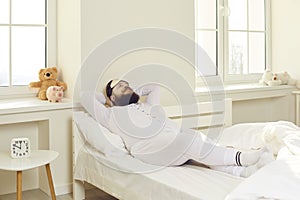 Funny bearded fat man in pajamas and sleeping mask lying on bed and dreaming