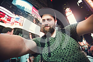 Funny bearded man backpacker smiling and taking selfie photo on Times Square in New York while travel across USA