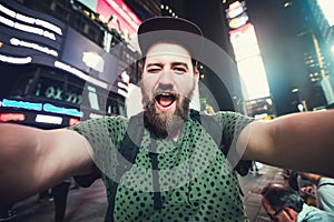 Funny bearded man backpacker smiling and taking selfie photo on Times Square in New York while travel across USA