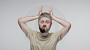 Funny bearded man doing antler gesture, bull horns on his head and looking at camera with menace expression