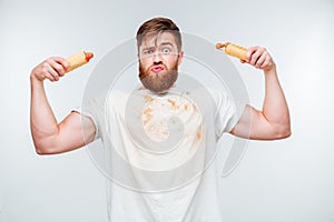Funny bearded man in filthy shirt holding to hotdogs