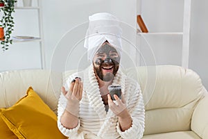 Funny bearded man having fun with a cosmetic mask on his face made from black clay. Men skin care, humor and spa at home