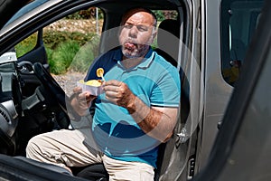 Funny bearded mature man eating vegan sandwich in the car. Unhealthy eating. Fast food. Takeaway food