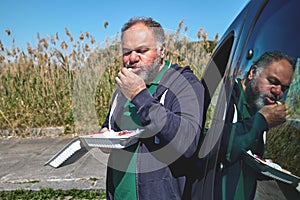 Funny bearded mature man eating vegan sandwich on the street near the car. Unhealthy eating. Fast food. Takeaway food