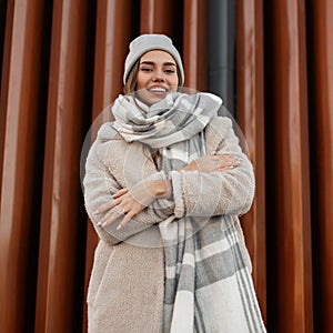 Funny beautiful young woman in a fashionable knitted hat in a stylish coat of milk color from eco-fur with a woolen warm scarf