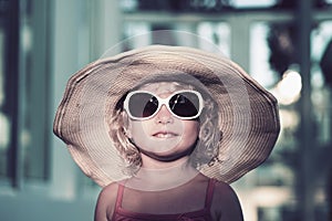 Funny blond little girl with a big hat and big sun glasses