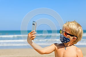 Funny boy in face mask taking selfie photo on beach