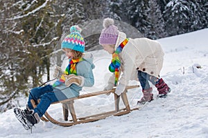 Funny boy and girl having fun with a sleigh in winter. Cute children playing in a snow. Winter activities for kids. Cold