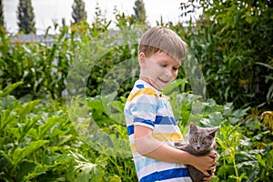 Funny boy hugging a cat with lots of love. Portrait of child holding on hands a Kitten. Playing with a cat on village countryside