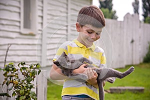 Funny boy hugging a cat with lots of love. Portrait of child holding on hands a Kitten. Playing with a cat on village countryside