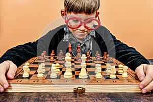 A funny boy in red glasses does not know how to play chess