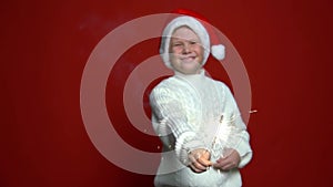 funny boy in Santa Claus cap holding sparkler on the red background. Concept Christmas