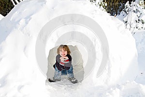 Funny boy in snow igloo on a sunny winter day