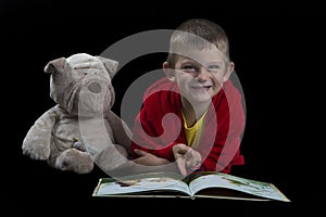 Funny boy with a stuffed dog reading a book for bed time