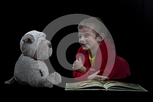 Funny boy with a stuffed dog reading a book for bed time