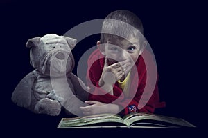 Funny boy with a stuffed dog reading a book for bed time in arti