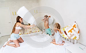 Funny brother and sister fighting pillow on bed morning bedroom kids boy and girl playing together