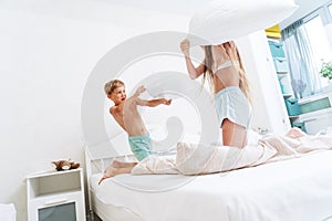 Funny brother and sister fighting pillow on bed morning bedroom kids boy and girl playing together