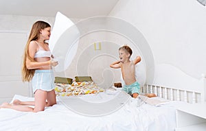 Funny brother and sister fighting pillow on bed morning bedroom kids boy and girl playing together