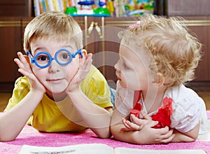 Funny brother in toy glasses with sister on floor
