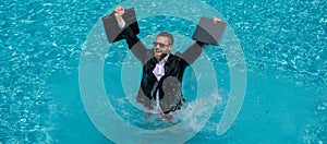 Funny business man in business suit with laptop jumping in splash water in the pool. Remote work. Crazy freelancer