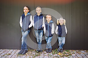 Funny Caucasian big family of three brothers and sister posing standing on growth background of wall in full growth. Equally