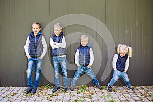 Funny Caucasian big family of three brothers and sister posing standing on growth background of wall in full growth. Equally