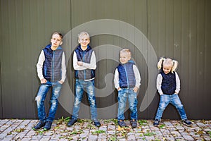 Funny Caucasian big family of three brothers and sister posing standing on growth background of wall in full growth. Equally