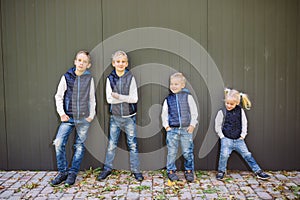 Funny Caucasian big family of three brothers and sister posing standing on growth background of wall in full growth. Equally