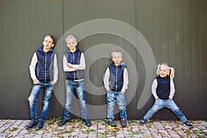 Funny Caucasian big family of three brothers and sister posing standing on growth background of wall in full growth. Equally