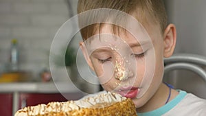 Funny Caucasian boy 6-7 years old with pleasure licks the cake. The boy got soiled with cake cream, licks a sweet dessert. A playf