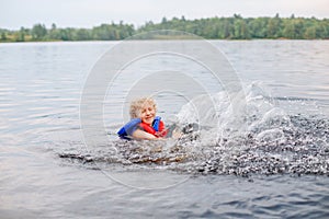 Funny Caucasian girl in lifeguard jacket swimming in lake. Child kid splashing in water river. Authentic candid lifestyle happy