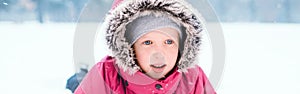 Funny Caucasian girl in warm winter clothes playing with snow. Cute child lying on ground during cold winter snowy day at snowfall photo