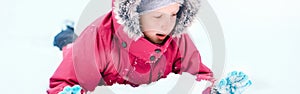 Funny Caucasian girl in winter clothes playing with snow. Cute child lying on ground during cold winter snowy day at snowfall.
