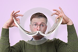 Funny caucasian male student in glasses holding book like a mustache