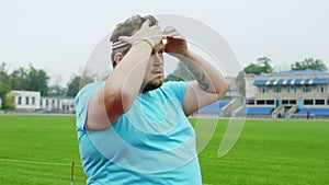 Funny and charismatic obese guy getting ready to start his workout time in the middle of stadium at the starting line he