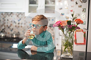 Funny charismatic retro style little boy in glasses drinking lemonade in kitchen