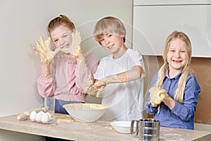 Funny cheerful children cook pizza in the kitchen. Children knead the dough.