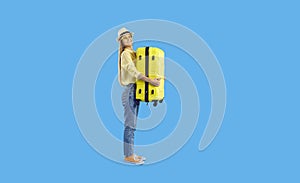 Funny cheerful girl traveler with yellow travel suitcase isolated on light blue background.