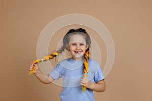 Funny cheerful joyful female child with missing tooth smiling looking at camera holding yellow kanekalon braids with