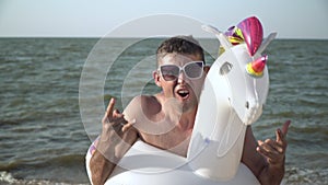 Funny cheerful man having fun at the sea. A man with a unicorn-shaped swimming ring on the beach