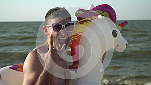 Funny cheerful man with an inflatable swimming ring in the shape of a unicorn on the sea beach