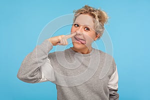 Funny cheerful woman with short hair in casual sweatshirt picking nose with stupid silly face, pulling out boogers