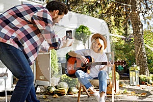 Funny and cheerful young couple. The girl plays the guitar, the guy photographs her for social networks against the