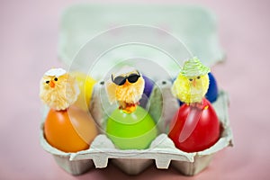 Funny chicks on colorful eggs in eggbox, pink background