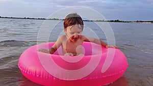 funny child boy sitting in pink inflatable ring and waving his hand to the camera hello, kid during summer vacation has