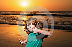 Funny child boy on sunset beach, thumbs up. Amazed surprised kids emotions.