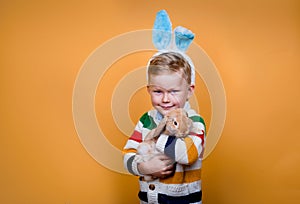 Funny child in bunny ears playing with rabbit. Little blond kid on Easter celebration. Egg hunt with pet animal