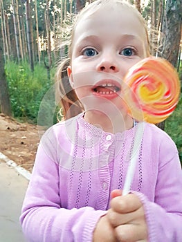 Funny child with candy lollipop, happy little girl eating big sugar lollipop, kid eat sweets. surprised child with candy