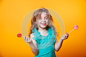 Funny child with candy lollipop, happy little girl eating big sugar lollipop on yellow bright background